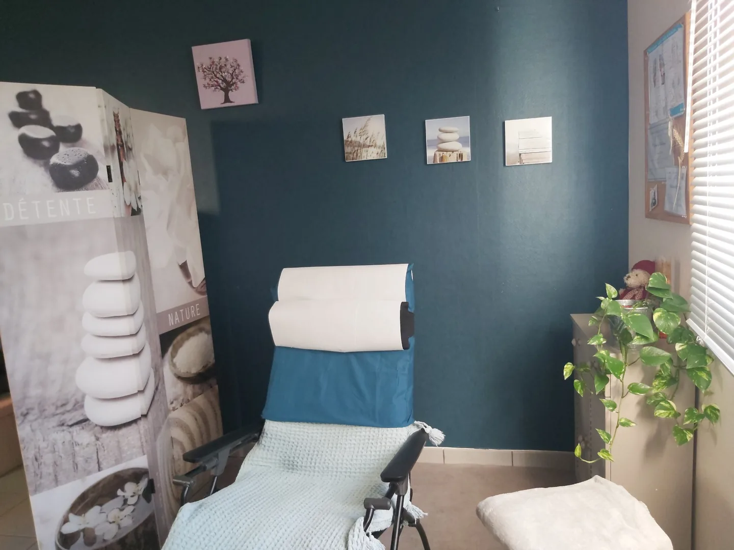 La salle de séance : le fauteuil relax et son plaid vert d'eau devant le mur bleu, à côté du paravent et de la planche de réflexologie.
